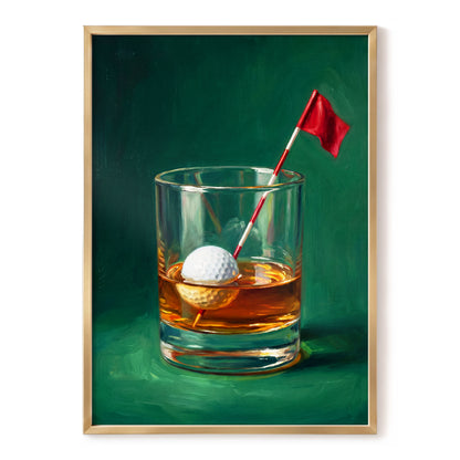 A framed art print depicting a still life of a whiskey glass with an amber drink, a white golf ball, and a small red flag on a dark green background, shown against a white wall.