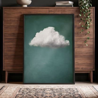 A framed vertical art print featuring a single fluffy white cloud against a deep teal-green background, leaning against a dark wood cabinet in a styled room with a hanging plant and patterned rug.