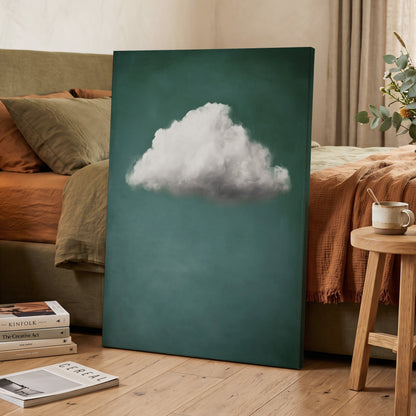 A vertical canvas wall art print leaning against a bed in a styled bedroom. The artwork features a large white cloud centered on a deep teal background.