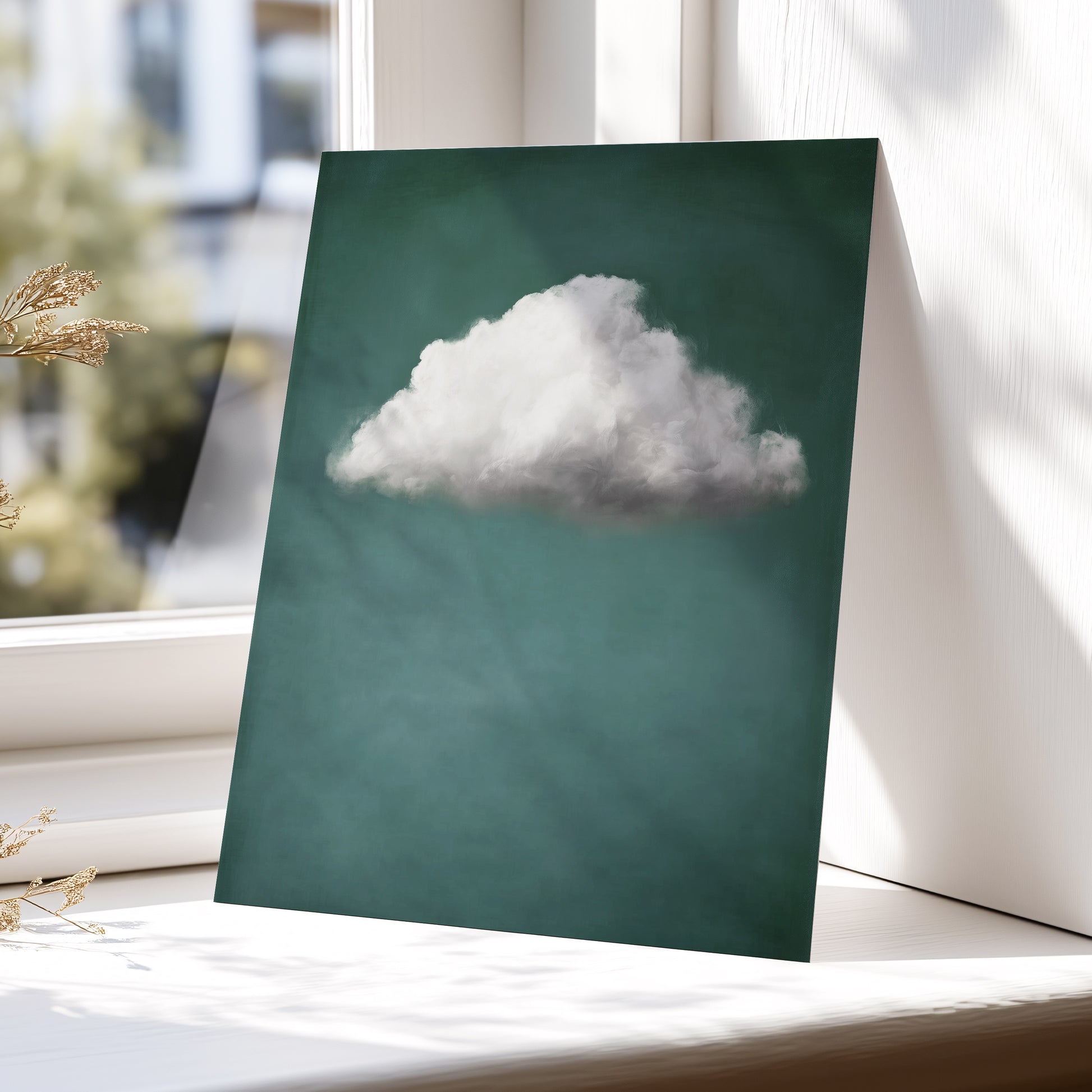 A vertical art print featuring a single fluffy white cloud against a deep teal-green background, leaning against a white window frame on a sunlit windowsill.