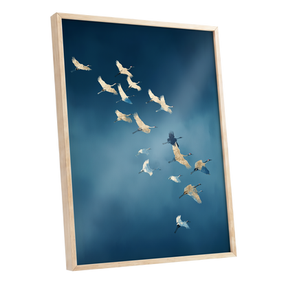 Framed wall art featuring a flock of cranes flying across a deep blue sky, shown in a light natural wood frame against a white background.