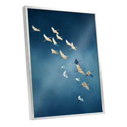 A framed wall art print showing a flock of cranes flying across a deep blue sky, displayed at an angle against a clean white background.