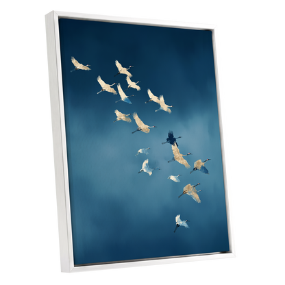 A framed vertical canvas print featuring a flock of cranes flying against a deep blue sky, shown at an angle with a white frame on a white background.