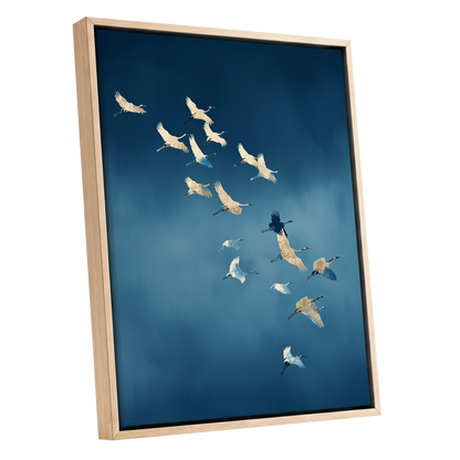 A framed wall art print depicting a flock of cranes flying across a deep blue sky, shown in a light natural wood frame against a white background.