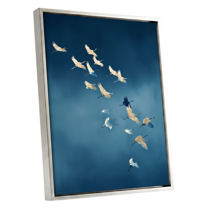 A framed wall art print showing a flock of cranes flying across a deep blue sky, presented at an angle with a silver frame on a white background.