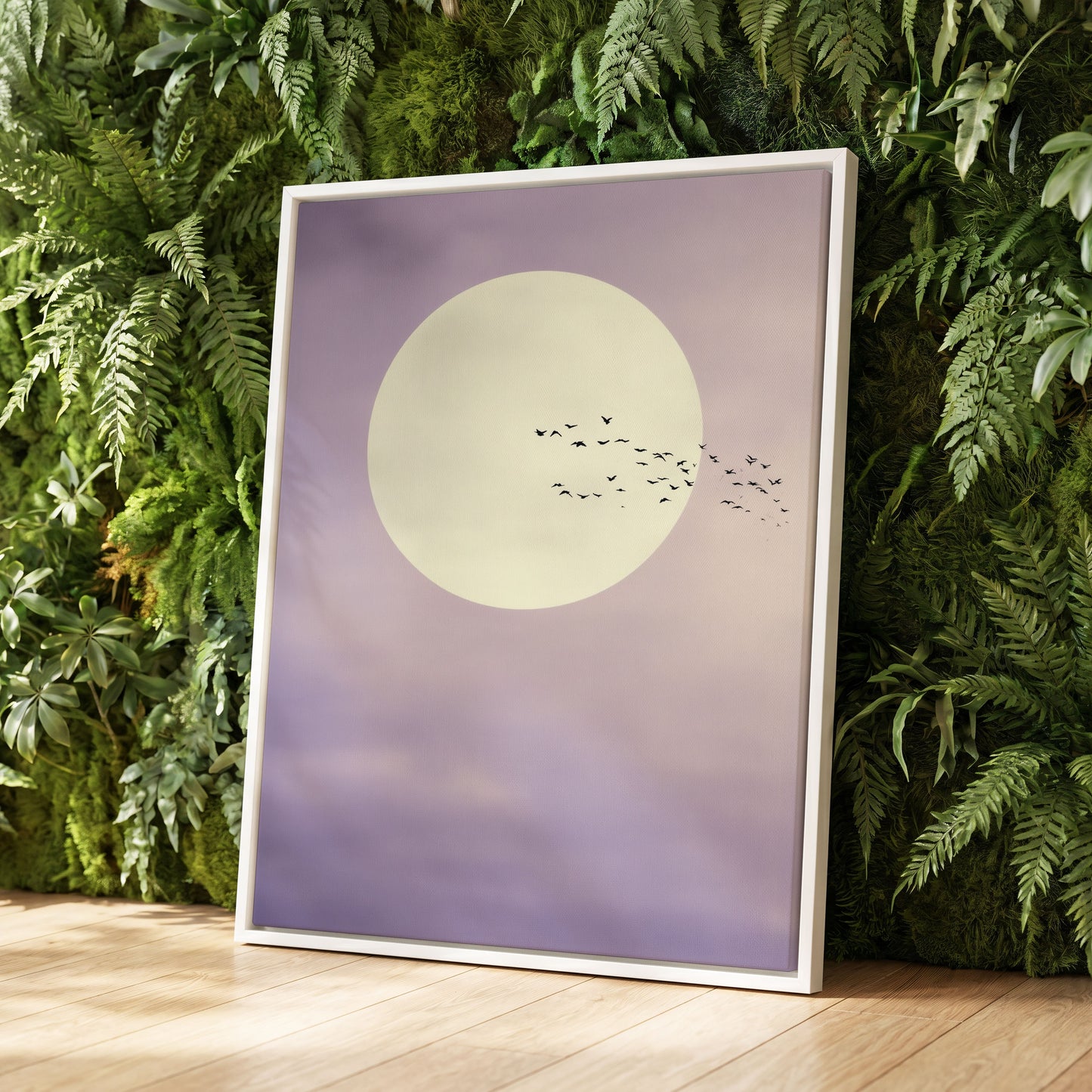 A framed art print featuring a large cream-colored moon and a flock of birds against a soft lavender-purple sky, leaning against a green fern wall on a light wood floor.