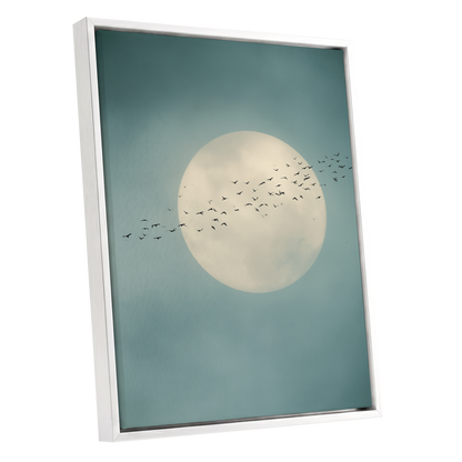 A framed art print featuring a large cream-colored full moon against a muted teal-blue sky, with a flock of small black birds flying across the center. The print is housed in a clean white frame and shown at a slight angle on a solid white background.