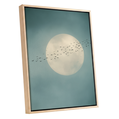 Framed wall art featuring a large cream full moon against a muted teal-blue sky, with a flock of small black birds flying across the center. The artwork is shown in a light natural wood frame on a plain white background.