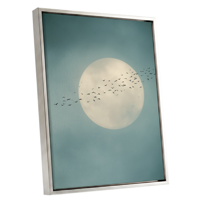 A framed art print featuring a large cream-colored full moon and a flock of birds against a muted teal-blue sky, housed in a modern silver frame.