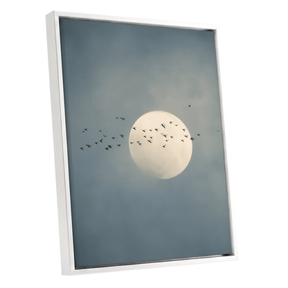 Framed wall art featuring a pale full moon against a muted blue-gray cloudy sky, with small black bird silhouettes flying around it. The artwork is shown in a white frame on a plain white background.