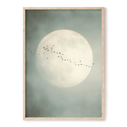 Framed wall art featuring a large pale full moon against a muted sage-gray sky, with a flock of small birds flying across the center, shown in a light natural wood frame on a white background.