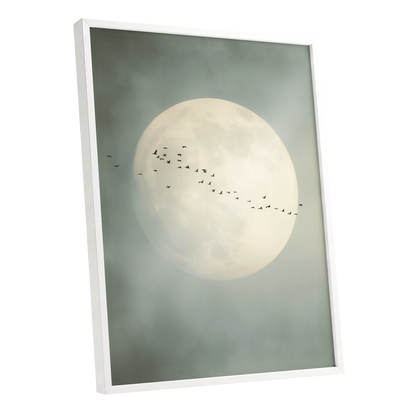 Framed wall art featuring a large pale full moon in a misty gray-green sky, with a line of small birds flying across the center. The frame is white and shown at a slight angle on a plain white background.