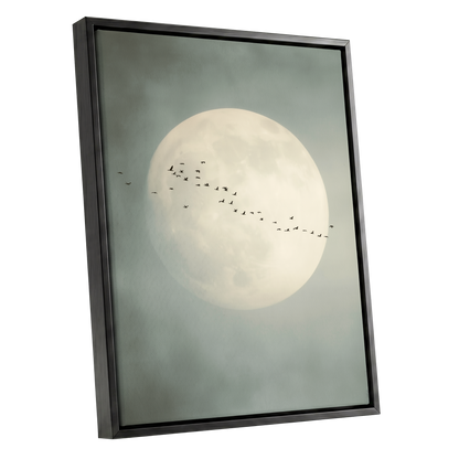 Framed wall art featuring a large pale full moon against a muted gray-green sky, with a small flock of birds across the center. The artwork is shown in a black frame at a slight angle on a plain white background.