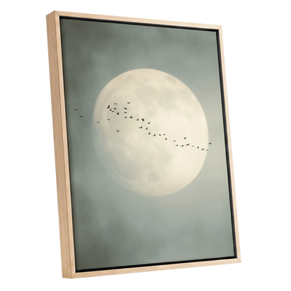 Framed wall art featuring a large pale full moon against a muted gray-green sky, with a line of small birds across the center. The artwork is shown in a light natural wood frame on a plain white background.