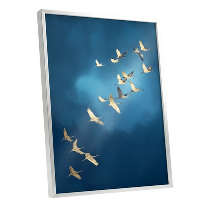 Framed wall art featuring a flock of white cranes flying across a deep blue sky, shown in a silver frame at an angle.