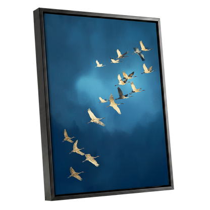 A framed wall art print showing a flock of cranes flying across a deep blue sky, presented at an angle with a black frame on a white background.