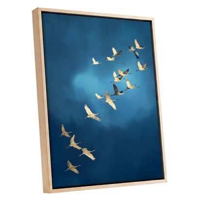 Framed wall art featuring a flock of cranes flying diagonally across a deep blue sky, shown in a light natural wood frame against a white background.