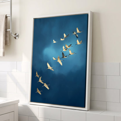 A framed vertical canvas print of a flock of cranes flying against a deep blue sky, leaning against a bathroom wall with white subway tiles.