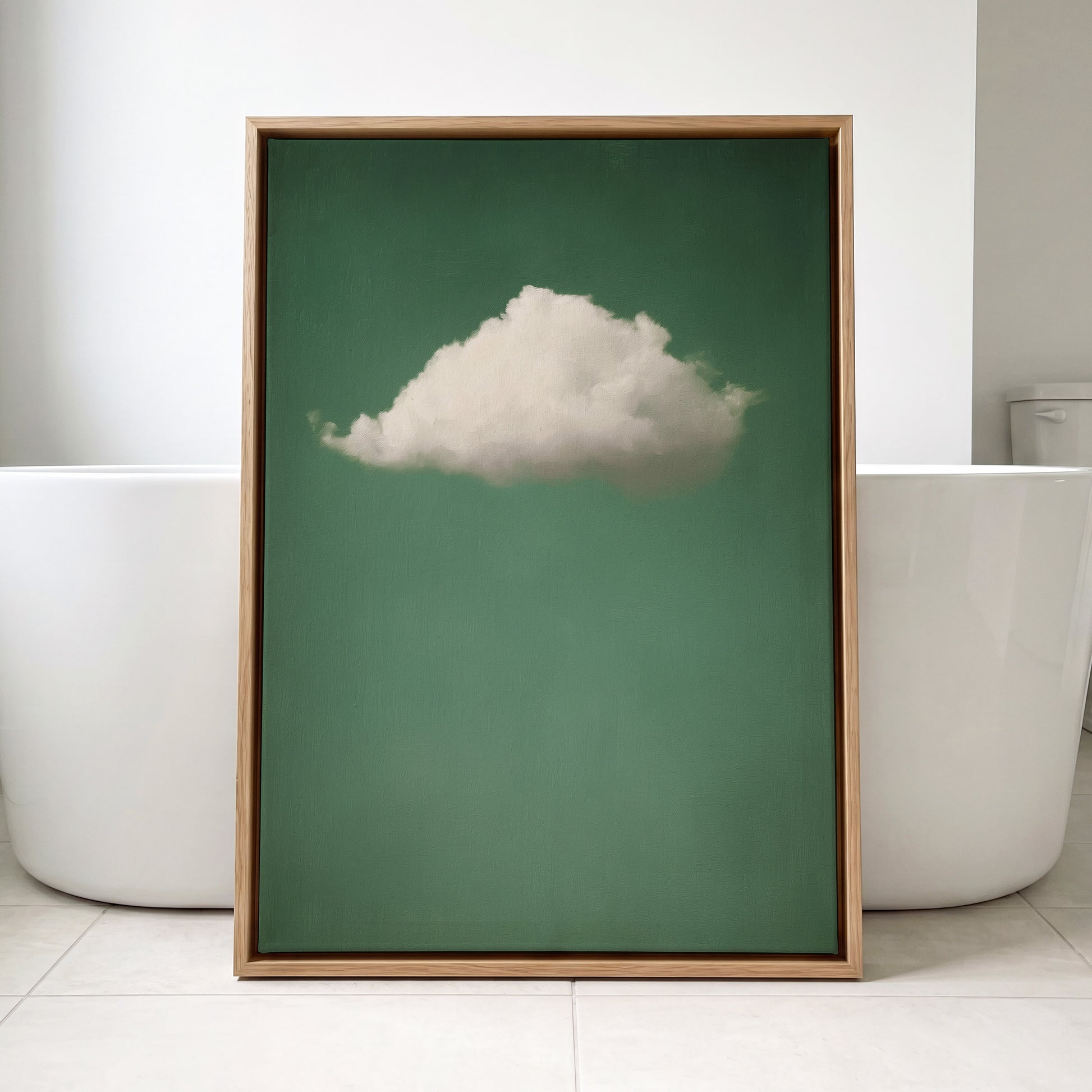 A framed art print featuring a single white cloud against a solid green background, leaning against a white bathtub in a bright bathroom setting.