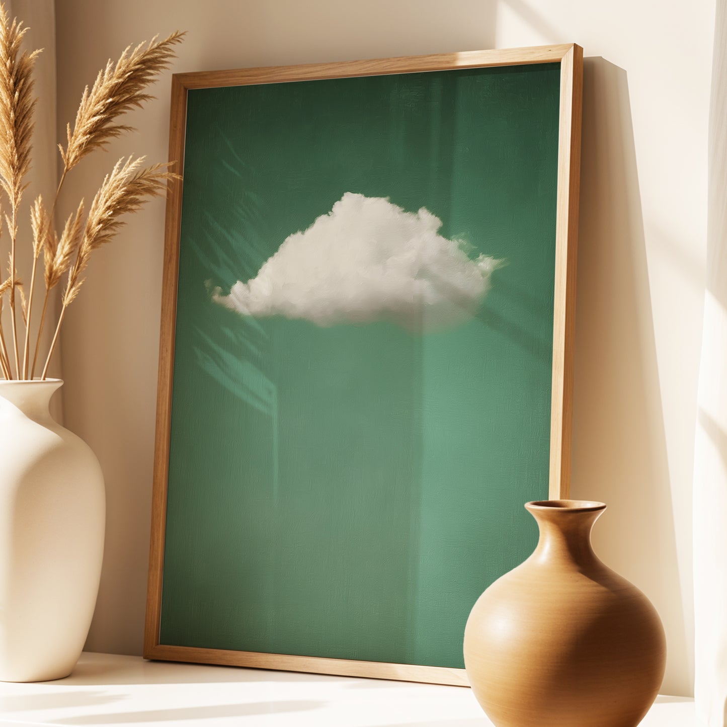 A framed art print featuring a single white cloud against a deep green background, styled in a warm interior setting with a wooden frame, flanked by two ceramic vases.