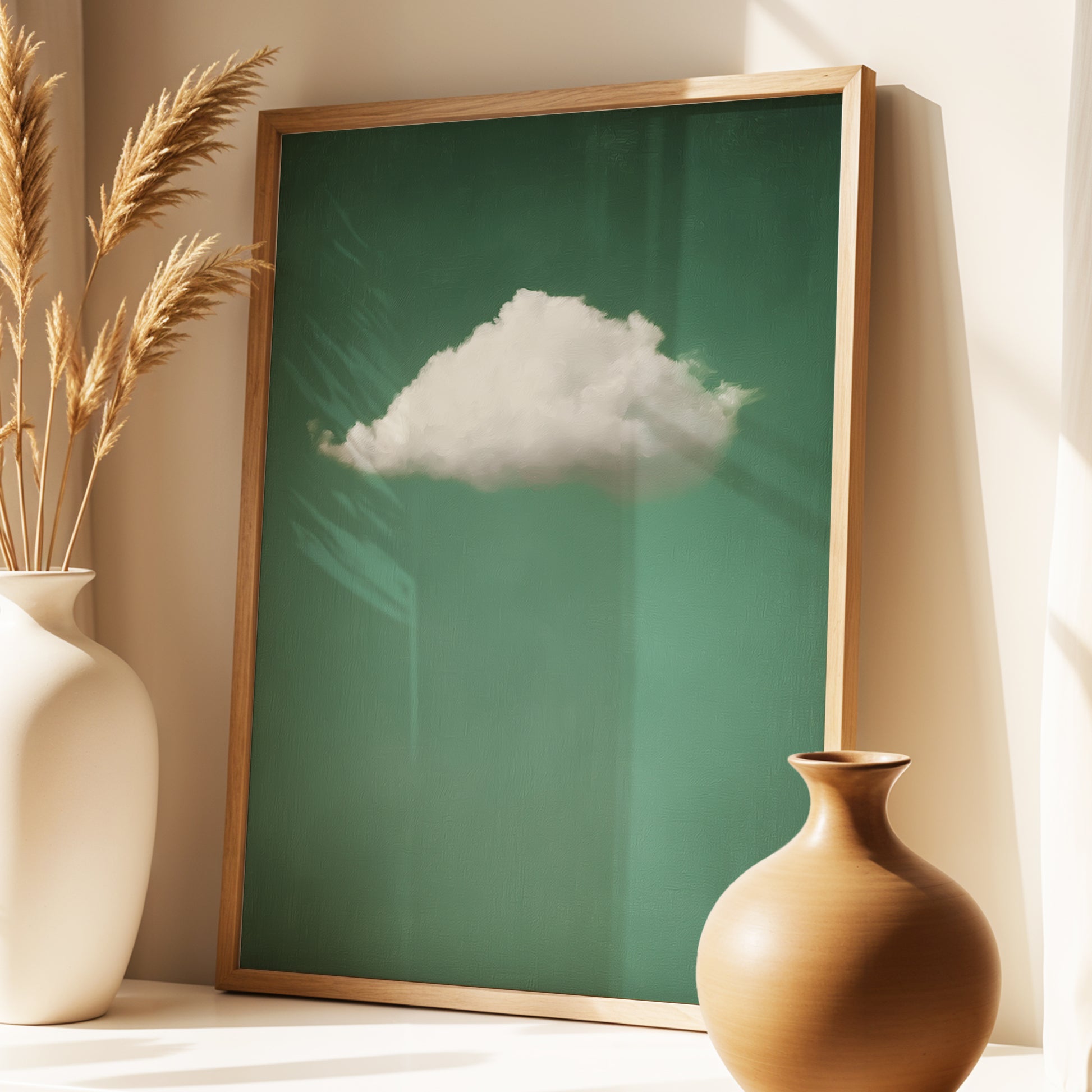 A framed art print featuring a single white cloud against a deep green background, styled in a warm interior setting with a wooden frame, flanked by two ceramic vases.