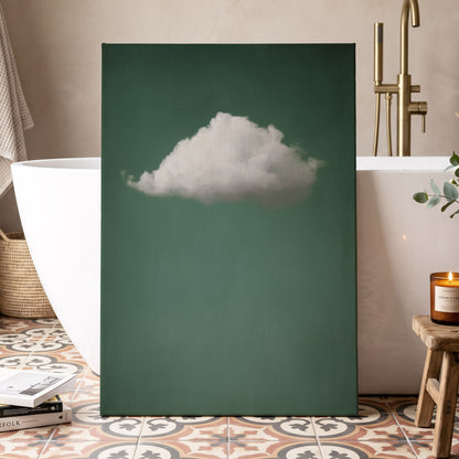 A vertical canvas wall art print featuring a single fluffy white cloud against a deep teal-green background, styled in a modern bathroom setting next to a white freestanding bathtub.