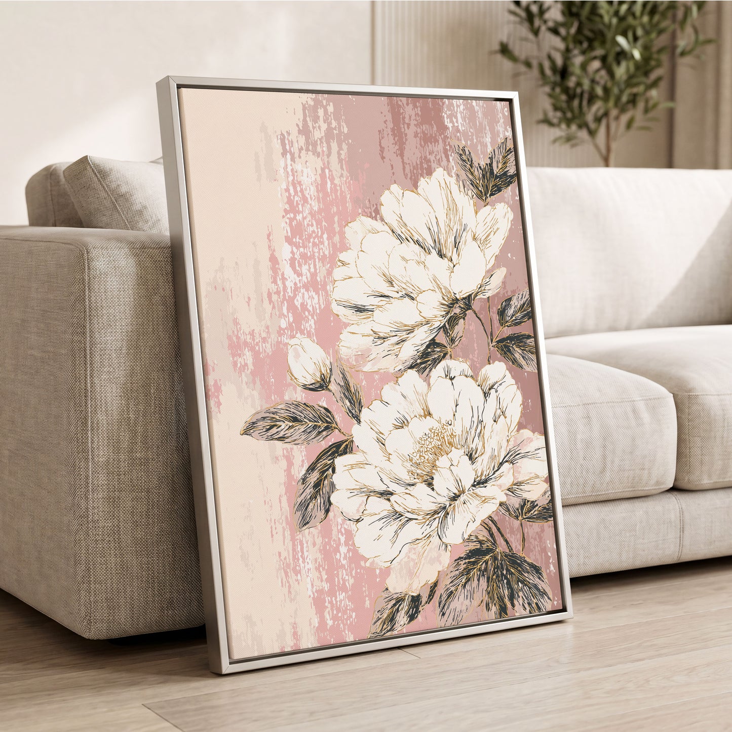 Blush Botanical Bloom: a framed floral wall art print leaning against a light beige sofa in a living room. The artwork features large cream-colored peony flowers with dark green leaves on a textured dusty pink background, enclosed in a thin silver frame.