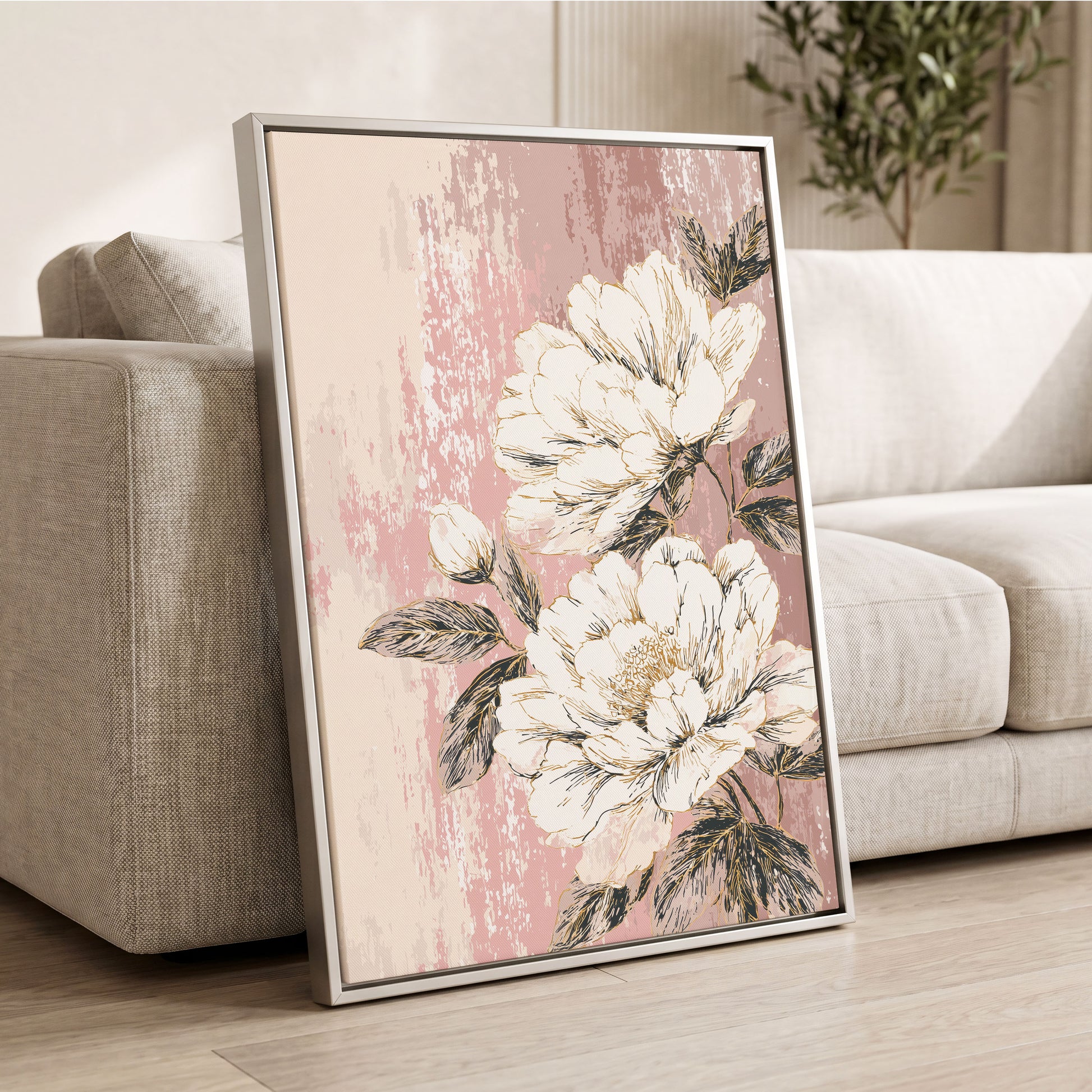 Blush Botanical Bloom: a framed floral wall art print leaning against a light beige sofa in a living room. The artwork features large cream-colored peony flowers with dark green leaves on a textured dusty pink background, enclosed in a thin silver frame.