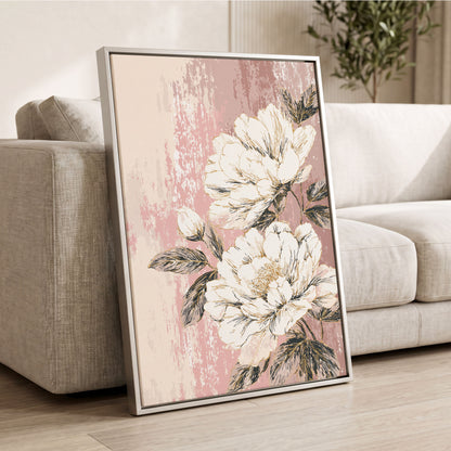 Blush Botanical Bloom: a framed floral wall art print leaning against a light beige sofa in a living room. The artwork features large cream-colored peony flowers with dark green leaves on a textured dusty pink background, enclosed in a thin silver frame.