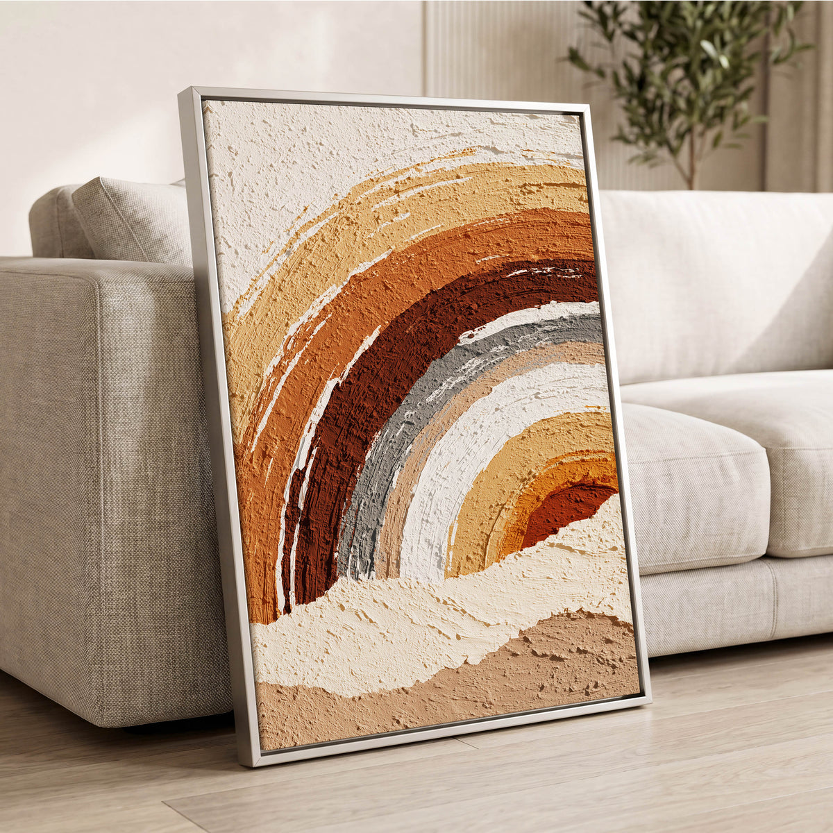 Earthtone Painted Arches: slim silver-framed textured abstract artwork in ochre, rust, brown, grey and cream, leaning beside a neutral sofa in a bright modern living room.