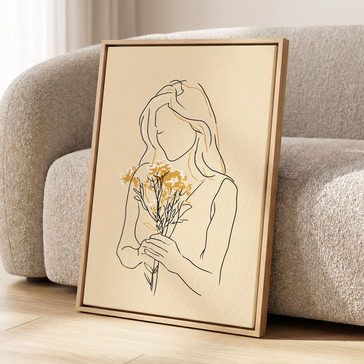 Golden Floral Silhouette: a framed minimalist line art print of a woman holding yellow flowers, leaning against a textured beige sofa on a light wood floor.
