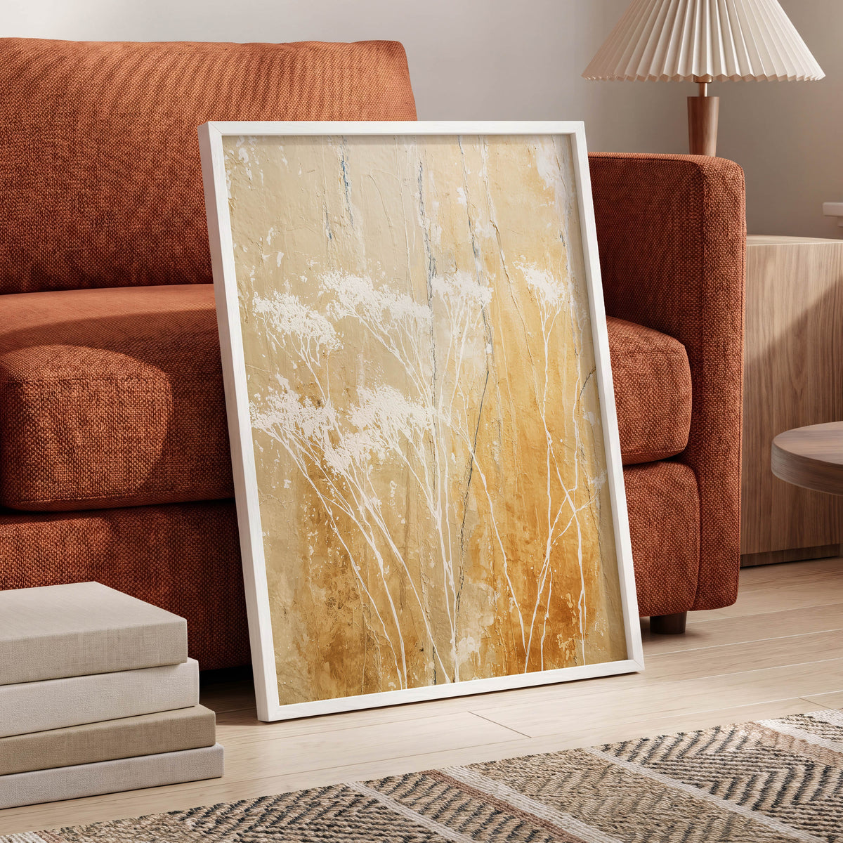 Golden Meadow Texture: a framed abstract floral art print with white blossoms on a warm gold and beige background, leaning against an orange-brown sofa in a styled living room.