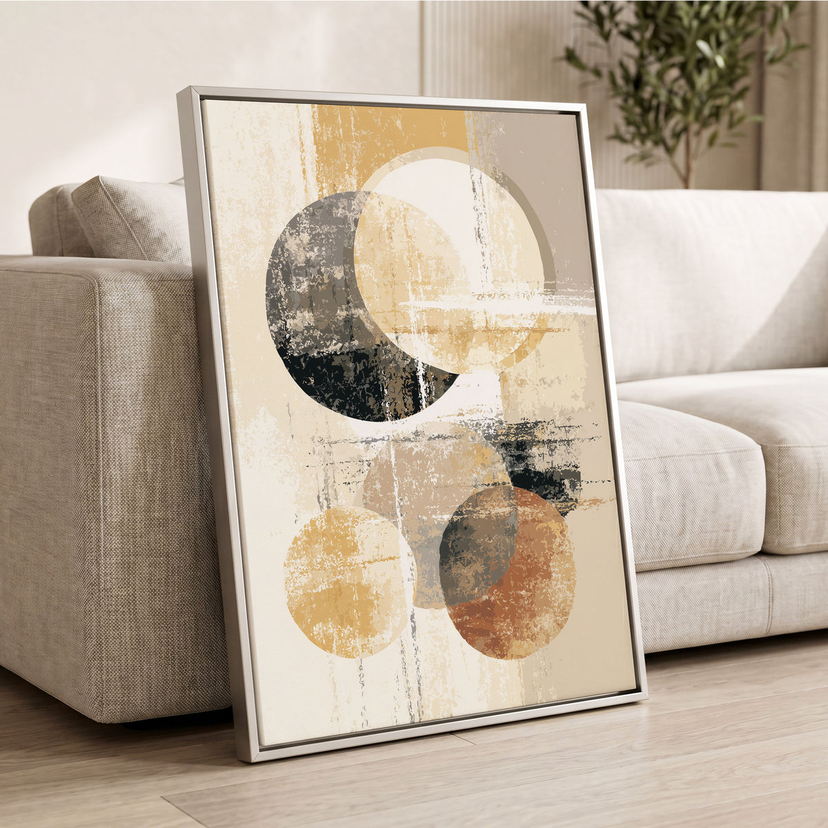 Neutral Orbit Abstract: a framed abstract art print with geometric circles in beige, black, and brown tones, leaning against a light gray sofa in a modern living room setting.