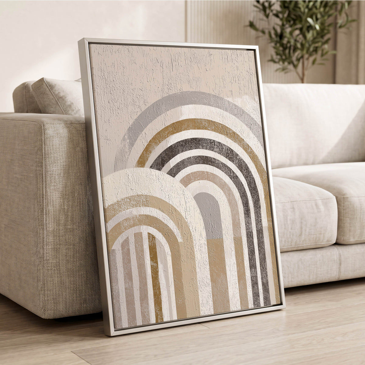 Neutral Rainbow Arches: a framed abstract art print with concentric arches in beige, gray, and white, leaning against a light beige sofa in a modern living room setting.