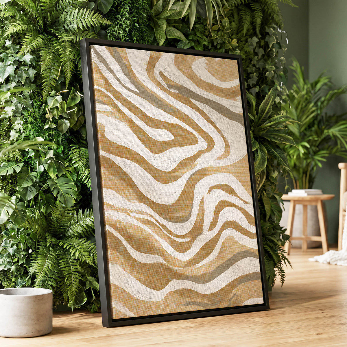 Ochre Flow Abstract: a framed abstract art print with wavy tan, beige, and cream lines in a black frame, leaning against a lush green leaf wall on a light wood floor.