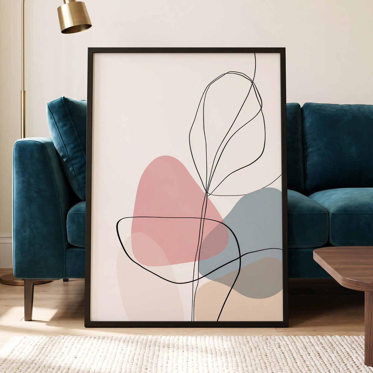 Pastel Botanical Lines: framed abstract botanical wall art leaning against a teal velvet sofa in a modern living room. The print features minimalist black line art over soft pink, dusty blue, and beige organic shapes on a warm off-white background.