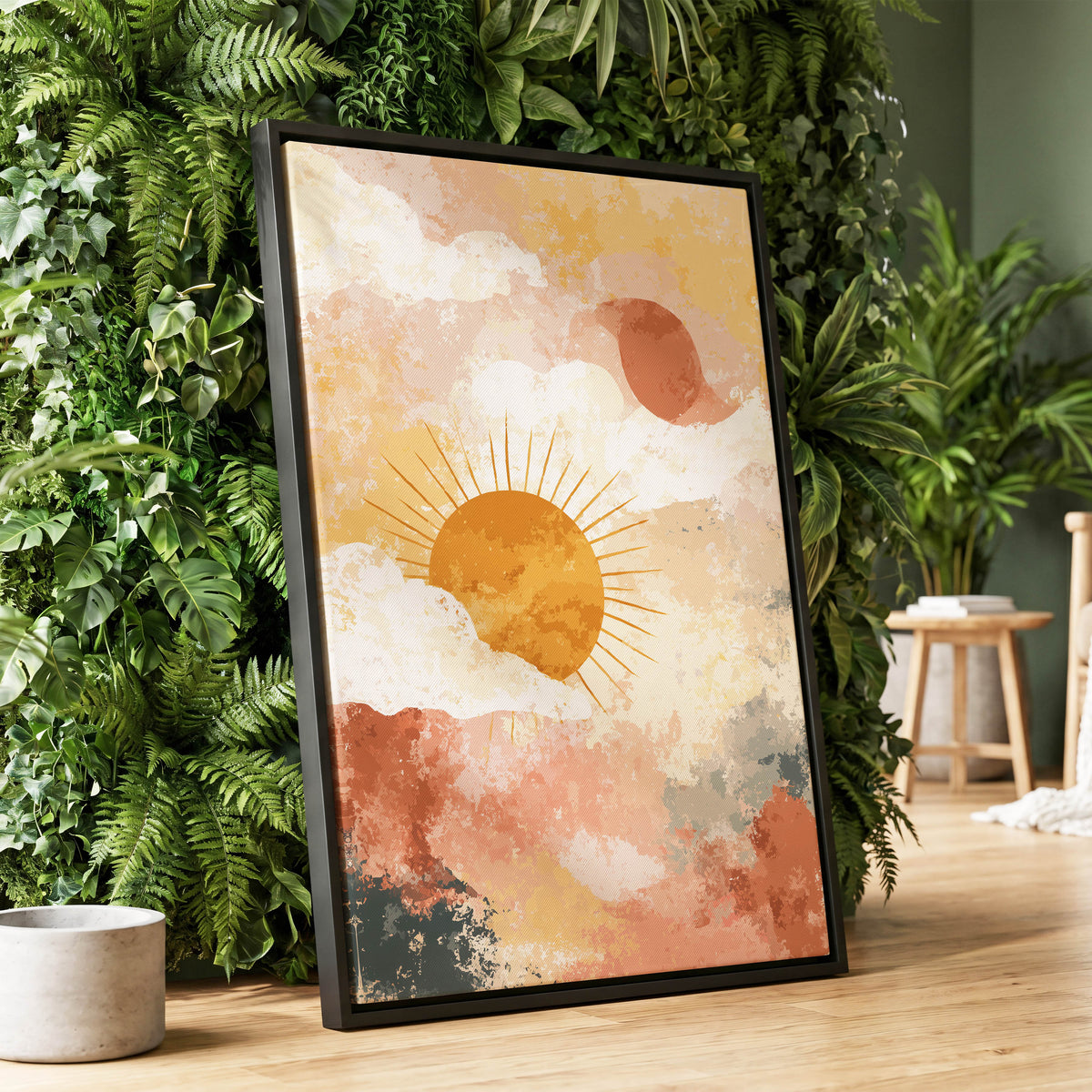 Pastel Sunrise Clouds: a framed art print featuring a stylized sun and clouds in warm earthy tones, leaning against a lush green wall on a wooden floor.